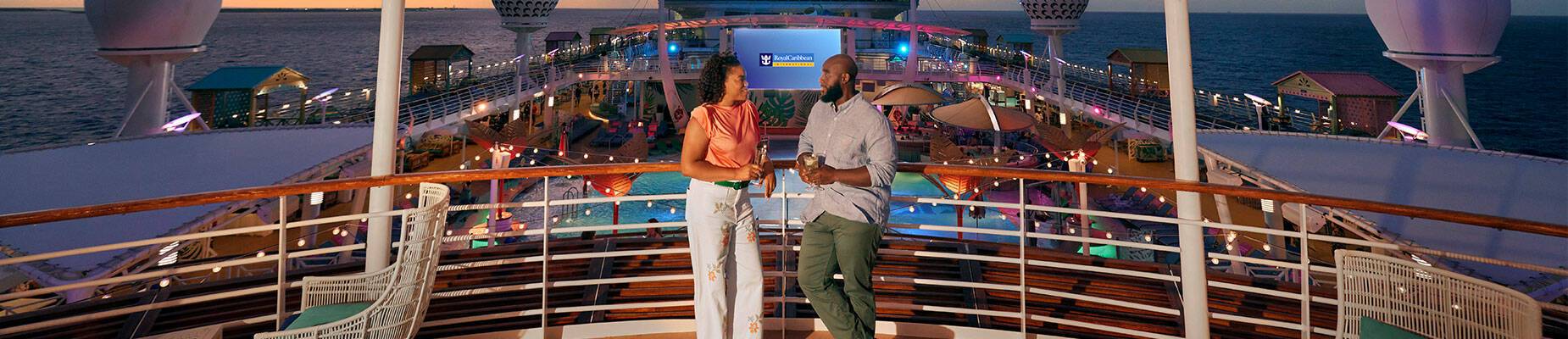A couple standing on a cruise ship deck with a drink in hand