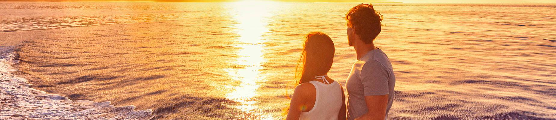 Couple on a cruise ship deck looking out at the sun setting
